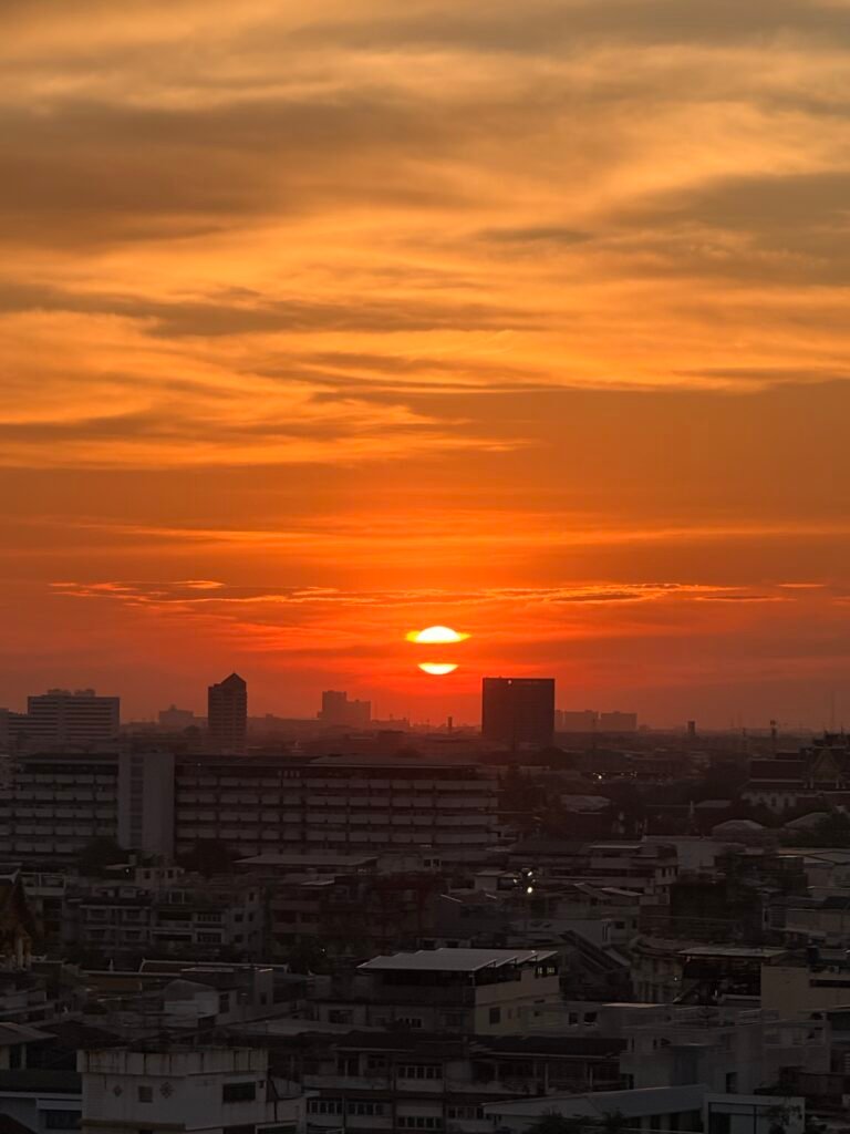 A dramatic sunset over the Bangkok city skyline with vivid orange and red sky as the sun sets behind the buildings